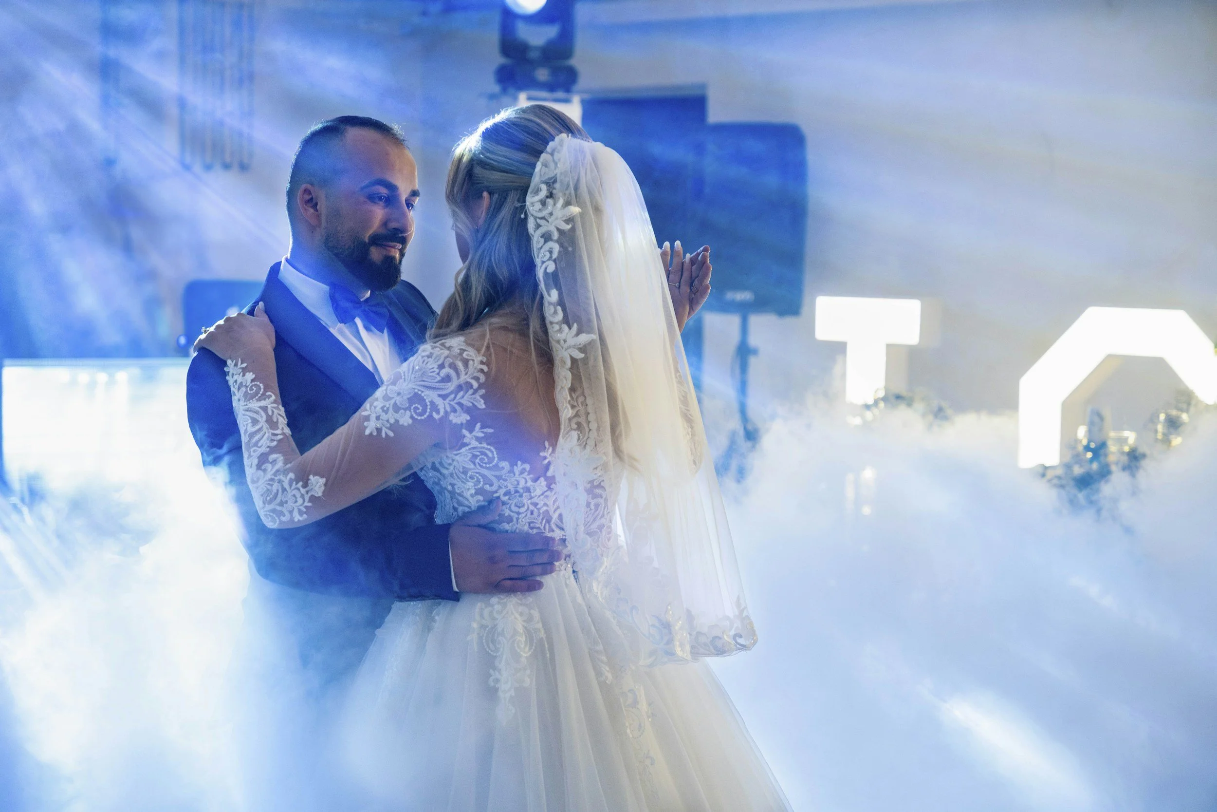 A bride and groom dancing during their wedding with fog effects, soft lighting, and illuminated décor in the background.